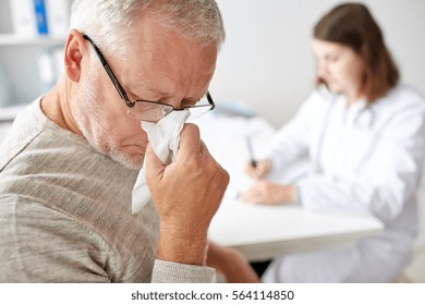 Medicine, Age, Health Care, Flu And People Concept - Close Up Of Senior Man Blowing Nose With Napkin And Doctor At Medical Office At Hospital