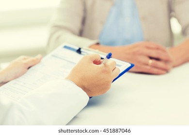 Medicine, Age, Health Care And People Concept - Close Up Of Senior Woman And Doctor Hands With Clipboard Meeting In Medical Office