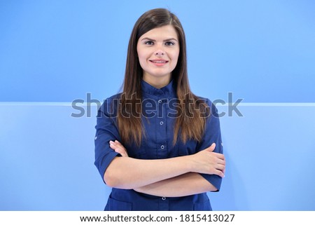 Medicine, beauty, dentistry, cosmetology, plastic surgery, confident business portrait of young smiling woman in blue uniform with arms crossed looking at camera on background of clinic
