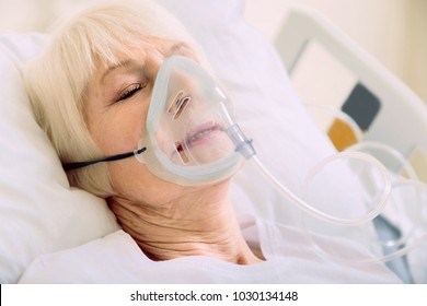 Medicine Is The Best Medicine. Ill Senior Woman Lying In A Hospital Bed While Wearing An Oxygen Mask And Undergoing Treatment.