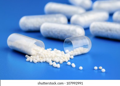 Medicine closeup: group of capsules, one of them broken up, on blue with shallow focus