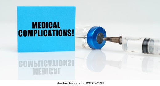 Medicine concept. On a white reflective surface are a syringe, an injection and a blue plaque that says - Medical Complications