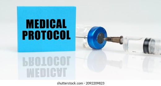 Medicine Concept. On A White Reflective Surface Are A Syringe, An Injection And A Blue Plaque That Says - Medical Protocol