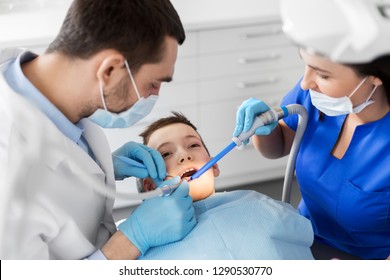 medicine, dentistry and healthcare concept - dentist and assistant with dental drill and saliva ejector treating kid patient teeth at dental clinic - Powered by Shutterstock