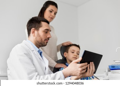 Medizin, Zahnheilkunde und Gesundheitskonzept - Zahnarzt, der dem Kind und seiner Mutter in der Zahnklinik einen Computer mit Tablette PC zeigt