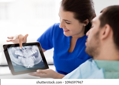 medicine, dentistry and healthcare concept - female dentist with tablet pc computer showing teeth x-ray to male patient at dental clinic office