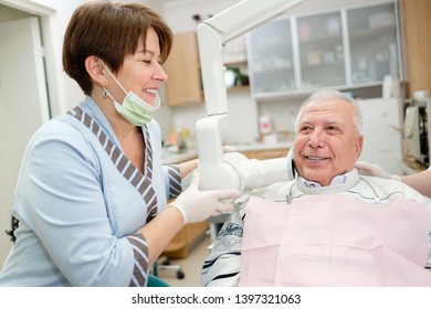 Medicine, Dentistry And Healthcare Concept - Female Dentist With X-ray Machine Scanning Senior Man 65-70 Years Old Patient Teeth At Dental Clinic. Radiography Procedure And Dental Care For Older Male