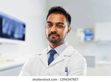 medicine, dentistry and healthcare concept - indian male dentist in white coat over dental clinic office background