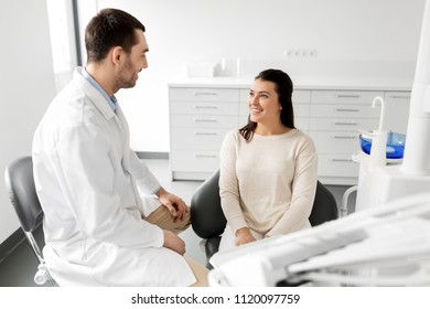 medicine, dentistry and healthcare concept - male dentist talking to female patient and discussing teeth treatment at dental clinic office - Powered by Shutterstock