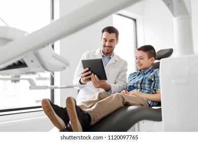 Medicine, Dentistry And Healthcare Concept - Smiling Male Dentist Showing Tablet Pc Computer To Kid Patient At Dental Clinic