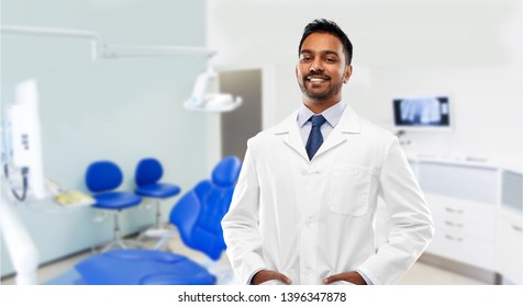 Medicine, Dentistry And Profession Concept - Smiling Indian Male Dentist In White Coat Over Dental Clinic Office Background