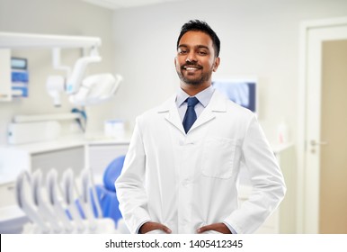 Medicine, Dentistry And Profession Concept - Smiling Indian Male Dentist In White Coat Over Dental Clinic Office Background