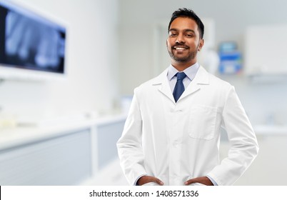 Medicine, Dentistry And Profession Concept - Smiling Indian Male Dentist In White Coat Over Dental Clinic Office Background