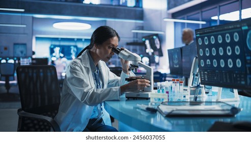 Medicine Development Laboratory: Asian Female Scientist Using Microscope, Analyzes Petri Dish Sample. Big Pharmaceutical Lab with Specialists Conducting Biotechnology Research, Developing New Drugs. - Powered by Shutterstock