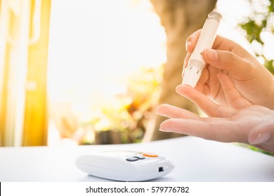 Medicine, Diabetes, Glycemia, Health care and people concept - close up of female using lancelet on  finger to checking blood sugar level by Glucose meter