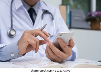 Medicine doctor with stethoscope holding pen, using mobile smart phone, reading anatomy textbook and holding pen in doctor room. Medical student browsing internet on smartphone.