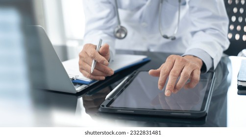 Medicine doctor working on digital tablet and laptop computer searching the information with medical document on table, close up. Doctor writing prescription and filling health insurance document - Powered by Shutterstock