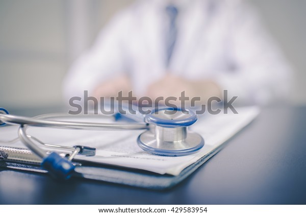 Medicine doctor\'s working table. Focus on blue\
color stethoscope vintage tone.\
