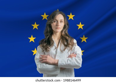 Medicine in European Union. Happy beautiful female doctor in medical coat standing with crossed arms against the background of the flag of European Union.