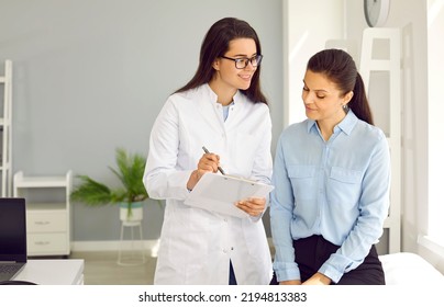 Medicine. Female doctor writes prescription or makes notes in female patient's card during medical examination. Friendly young nurse and woman talking in doctor's office in modern medical clinic. - Powered by Shutterstock