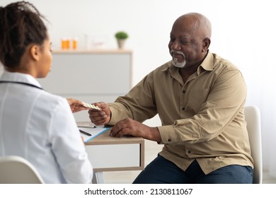Medicine And Health Care Concept. Black female doctor giving elderly male patient pills, man holding tablets. Young specialist prescribing treatment to mature adult taking painkiller or vitamins - Powered by Shutterstock