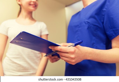 Medicine, Health Care And People Concept - Close Up Of Female Doctor Or Nurse Holding Clipboard With Pen And Talking To Girl At Hospital