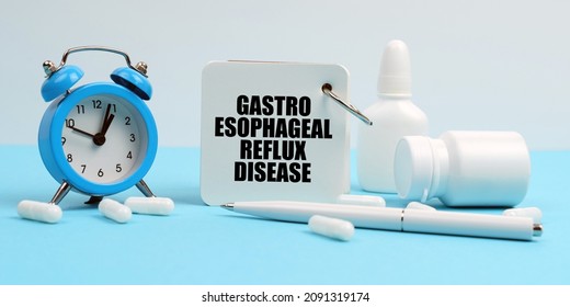 Medicine And Health Concept. On A Blue Surface Lie Pills, An Alarm Clock And A Notebook With The Inscription - Gastro Esophageal Reflux Disease