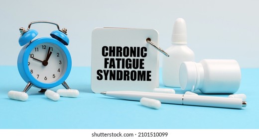 Medicine and health concept. On a blue surface lie pills, an alarm clock and a notebook with the inscription - Chronic Fatigue Syndrome