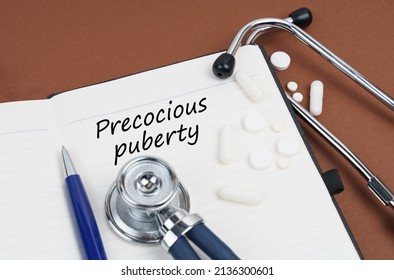 Medicine and health concept. On a brown surface lie pills, a pen, a stethoscope and a notebook with the inscription - Precocious puberty