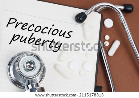 Medicine and health concept. On a brown surface lie pills, a stethoscope and a notebook with the inscription - Precocious puberty
