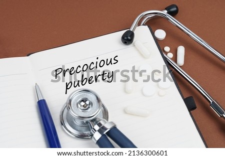 Medicine and health concept. On a brown surface lie pills, a pen, a stethoscope and a notebook with the inscription - Precocious puberty