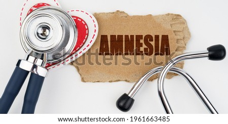 Medicine and health concept. On a white table lie a heart, a stethoscope and a cardboard with the inscription - Amnesia