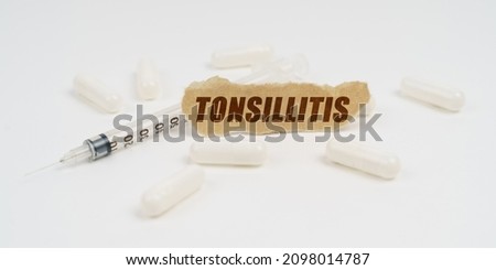 Medicine and health concept. On a white table are pills, a syringe and a piece of paper with the inscription - Tonsillitis