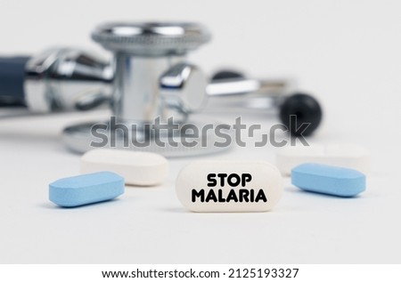 Medicine and health concept. On a white surface lie pills, a stethoscope and a tablet with the inscription - STOP MALARIA