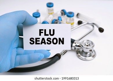 Medicine And Health Concept. A Stethoscope And Ampoules Lie On A White Background, The Doctor Holds A Business Card With The Inscription - FLU SEASON