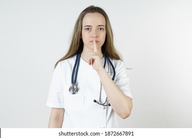 Medicine and health concept. A young woman doctor shows with a finger gesture that silence should be observed. Isolated on white background.