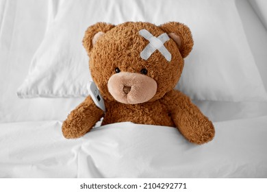 medicine, healthcare and childhood concept - ill teddy bear toy with medical patch on head and thermometer lying in bed - Shutterstock ID 2104292771