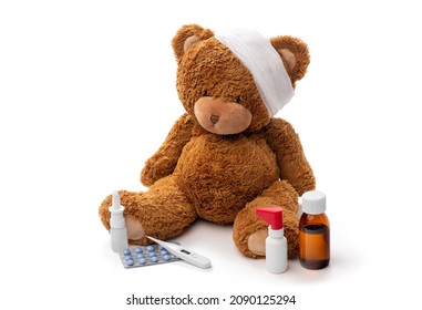 medicine, healthcare and childhood concept - teddy bear toy with bandaged head thermometer and drugs on white background