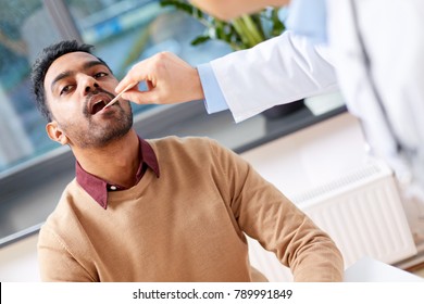 Medicine, Healthcare And Laryngology Concept - Doctor Or Laryngologist With Tongue Depressor Examining Male Patient Throat At Clinic