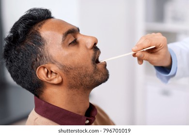 Medicine, Healthcare And Laryngology Concept - Doctor Or Laryngologist Hand With Tongue Depressor Examining Male Patient Throat At Clinic