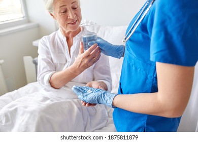 Medicine, Healthcare And Old Age Concept - Doctor Or Nurse Giving Pills And Glass Of Water To Smiling Senior Woman At Hospital Ward