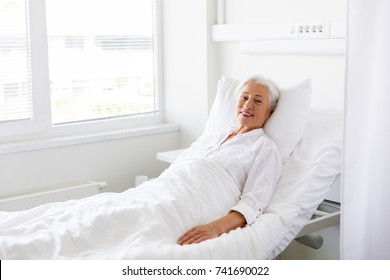 Medicine, Healthcare And Old People Concept - Smiling Senior Woman Lying On Bed At Hospital Ward