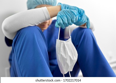 medicine, healthcare and pandemic concept - sad young female doctor or nurse holding face protective mask for protection from virus disease sitting on floor at hospital - Powered by Shutterstock