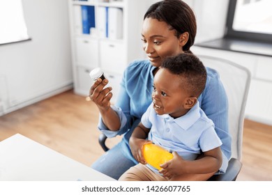 Medicine, Healthcare And Pediatry Concept - African American Mother With Baby Son Holding Medication At Clinic