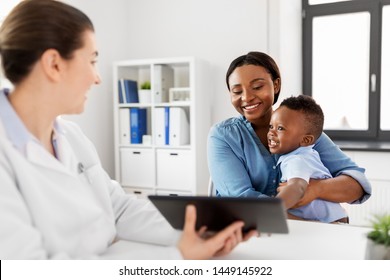 Medicine, Healthcare And Pediatry Concept - African American Mother With Baby Son And Caucasian Doctor With Tablet Computer At Clinic