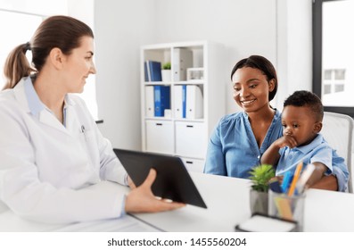 Medicine, Healthcare And Pediatry Concept - African American Mother With Baby Son And Caucasian Doctor With Tablet Computer At Clinic