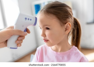 medicine, healthcare and pediatry concept - female doctor's or pediatrician's hand measuring little girl patient's temperature with infrared forehead thermometer at clinic
