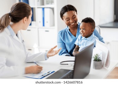 Medicine, Healthcare And Pediatry Concept - Happy African American Mother With Baby Son And Caucasian Doctor At Clinic