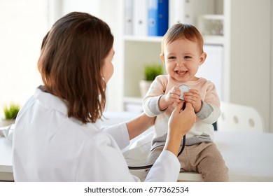 Medicine, Healthcare, Pediatry And People Concept - Doctor With Stethoscope Listening To Happy Smiling Baby Girl On Medical Exam At Clinic