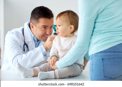 medicine, healthcare, pediatry and people concept - otolaryngologist or doctor checking baby ear with otoscope and young woman at clinic